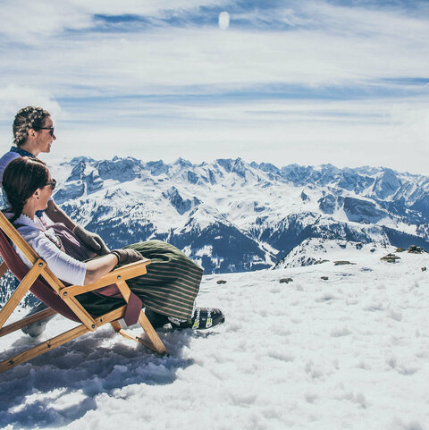 Zwei Frauen sitzen auf Holzstühlen im Schnee
