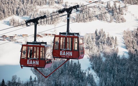 Zwei rote Gondeln mit verschneiter Landschaft im Hintergrund