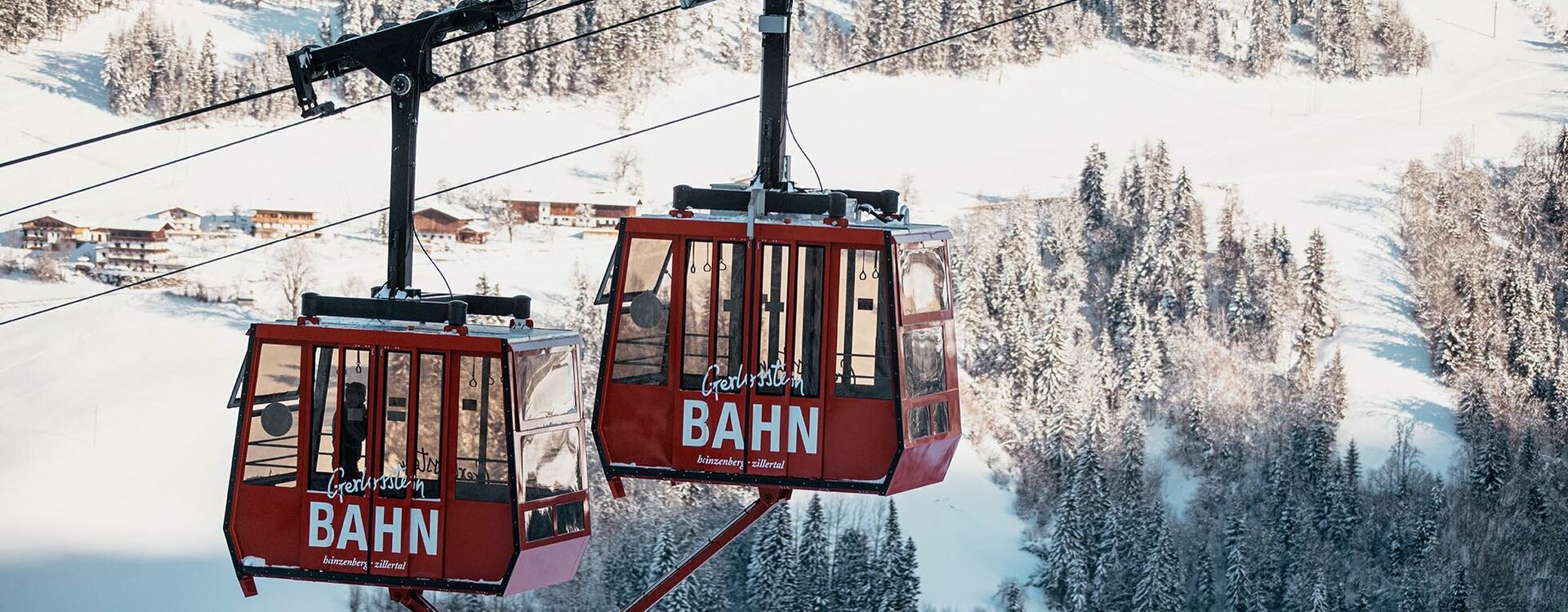 Zwei rote Gondeln mit verschneiter Landschaft im Hintergrund