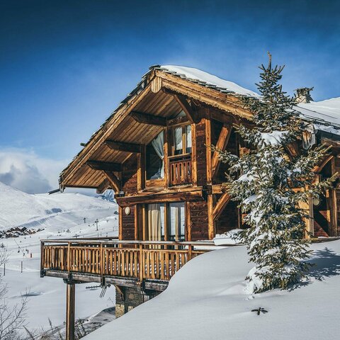 Holzhaus, das von Schnee bedeckt ist, mit winterlicher Atmosphäre und verschneiten Bäumen rundherum