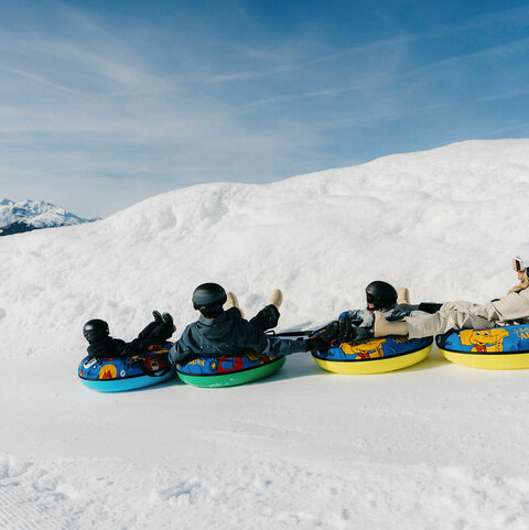 Vier Kinder auf bunten Snowtubing-Reifen in verschneiter Winterlandschaft.