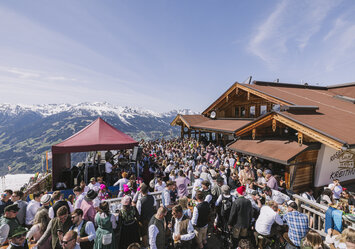 Viele Menschen in Trachtenkleidung feiern vor einem Haus.
