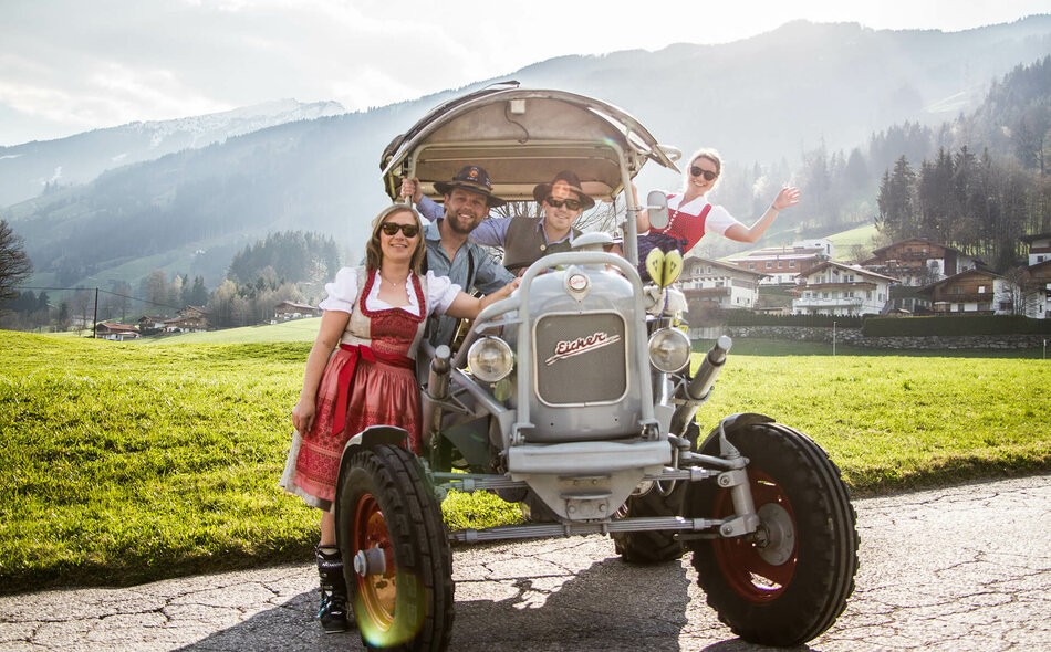 Zwei Männer und zwei Frauen in Trachtenkleidung sitzen auf einem Traktor