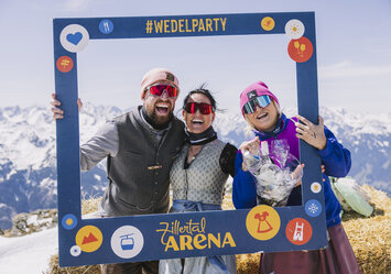 Ein Mann und zwei Frauen in Tracht posieren mit einem Bilderrahmen.