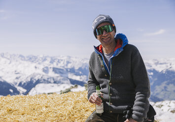 Ein Mann sitzt mit Bier in der Hand auf einem großen Heuballen.