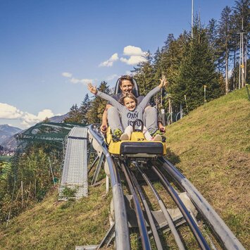 Ein Mann und ein Mädchen fahren mit einer Sommerrodelbahn.