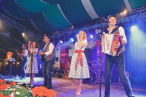 Drei Männer und zwei Frauen in Trachtenkleidung singen auf der Bühne