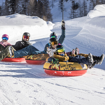 Eine Familie fährt auf Reifen die Piste hinunter