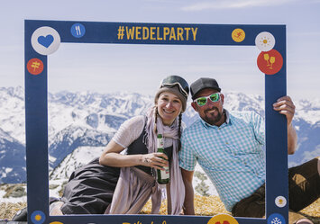Ein Mann und eine Frau sitzen auf einem großen Heuballen und posieren mit einem Bilderrahmen.