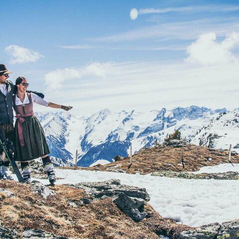 Ein Mann und eine Frau in Trachtkleidung stehen mit Skiern im Schnee