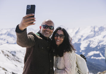 Ein Paar macht ein Selfie mit traumhafter Bergkulisse im Hintergund.
