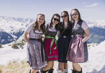 Vier Frauen in Trachtenkleidung posieren im Schnee für ein Foto.