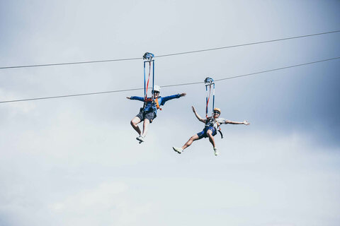 Zwei Personen fahren mit einer Zipline über der traumhaften Natur