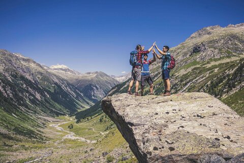 Drei Männer stehen auf einem Stein, mit einer traumhaften Bergkulisse im Hintergrund