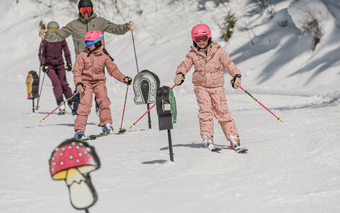 Eine Familie fäührt mit Skiern an Hindernissen auf einer verschneiten Skipiste vorbei.
