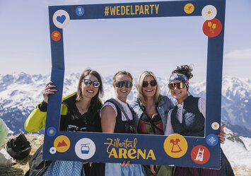 Vier Frauen in Trachtenkleidung posieren im Schnee mit einem Bilderrahmen.
