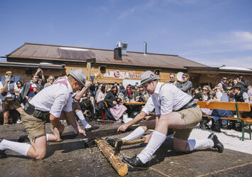 Drei Männer sägen und hacken ein langes Stück Holz.