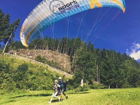 Zwei Personen beim Start eines Tandem-Paragliders auf einer Wiese.