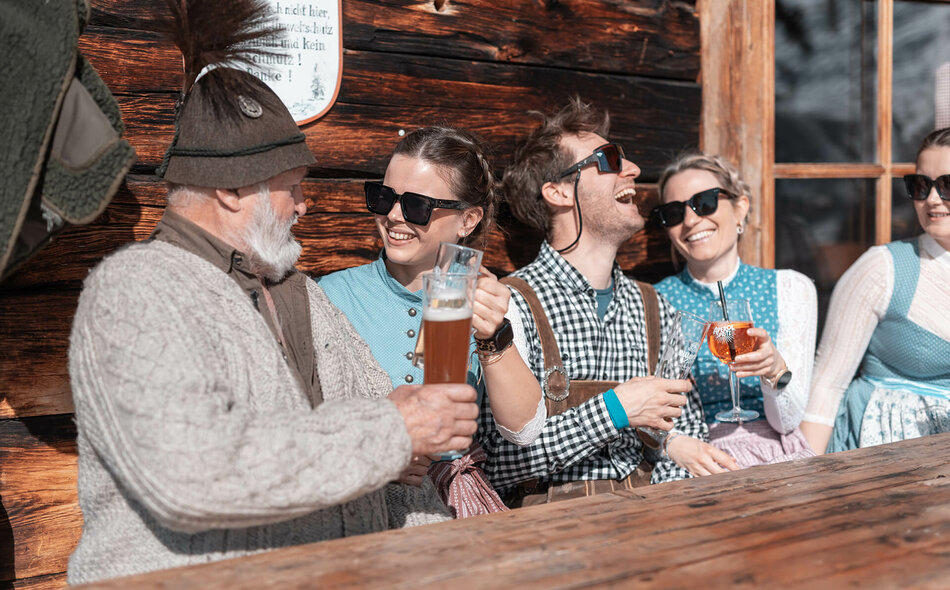 Männer und Frauen in Trachtenkleidung trinken Bier und Aperol bei einer Hütte