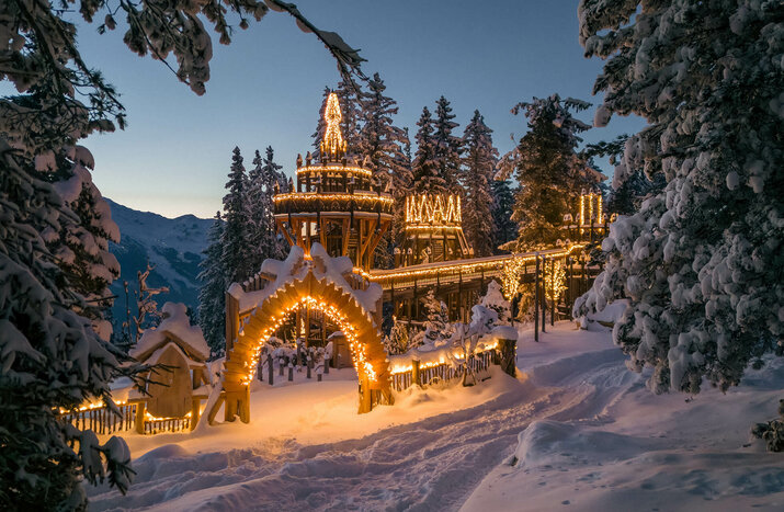 Festlich beleuchtetes Fichtenschloss im Winter, umgeben von verschneiten Bäumen und winterlicher Abendstimmung.