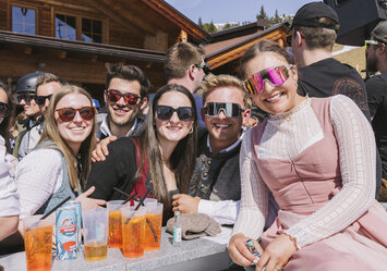 Zwei Männer und drei Frauen in Trachtenkleidung sitzen zusammen und trinken Aperol Spritz.