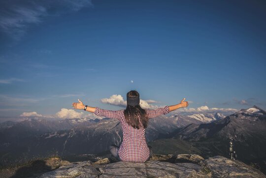 Eine Frau sitzt, mit ausgestreckten Händen, vor einer traumhaften Bergkulisse