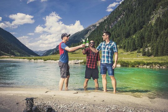 Drei Männer trinken ein Bier an einem See