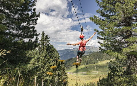 Eine Frau rutscht auf einer Seilrutsche durch eine grüne Landschaft.