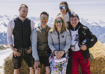 Fünf Personen in Tracht posieren für ein Foto auf einem Heuballen. 