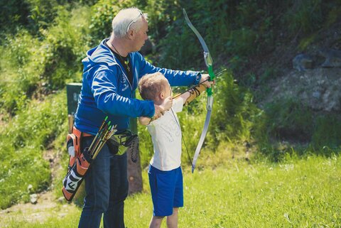 Ein älterer Mann unterstützt einen kleinen Jungen beim Bogenschießen.