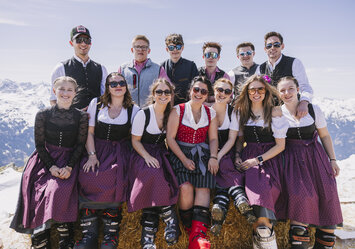 Personen in Tracht sitzen auf einem Heuballen und posieren für ein Foto.