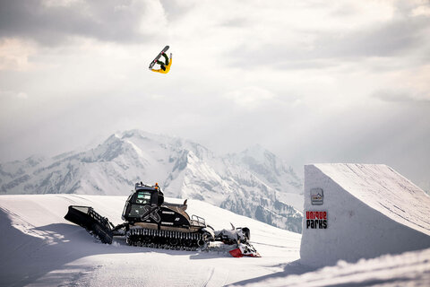 Ein Snowboarder macht einen Sprung über einem Pistenbully