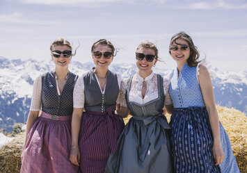 Vier Frauen in Dirndln sitzen auf einem großen Heuballen.