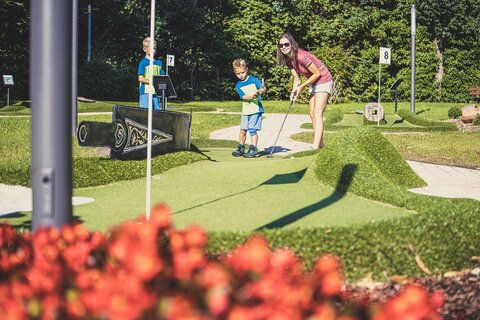 Eine Frau und zwei kleine Jungs spielen Minigolf