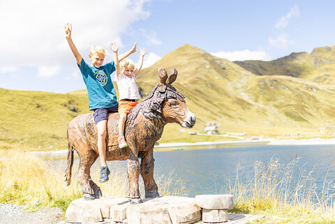 Zwei Kinder sitzen auf einer hölzernen Pferdestatue