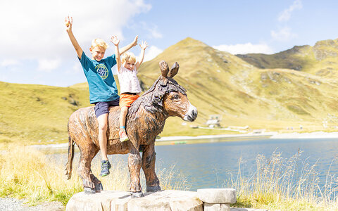 Zwei Kinder sitzen auf einer hölzernen Pferdestatue