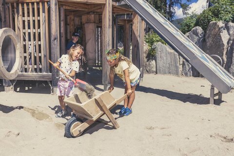 Kinder spielen mit Schaufel und Schubkarre im Sandkasten