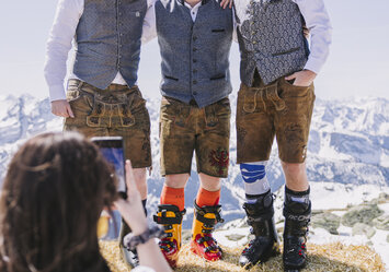 Drei Männer in Tracht stehen auf einem Heuballen und posieren für ein Foto.