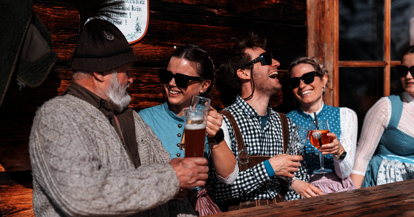 Frauen und Männer in Tracht trinken an einer Hütte.