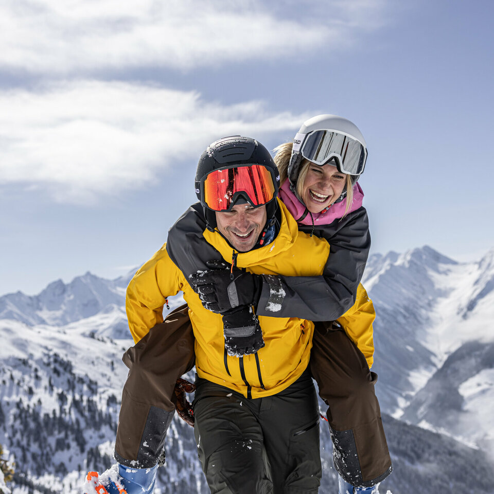 Lachender Mann schultert Frau auf der Piste