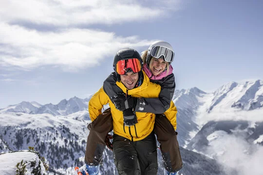 Lachender Mann schultert Frau auf der Piste