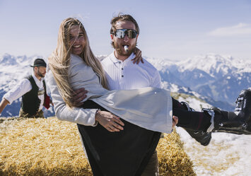 Ein Mann mit einer Zigarre im Mund trägt eine Frau auf den Händen.