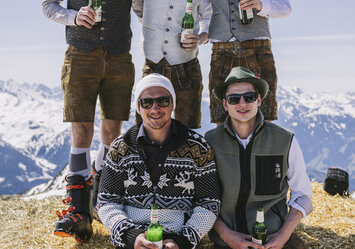 Fünf Männer mit Bier in der Hand sitzen auf einem Heuballen.